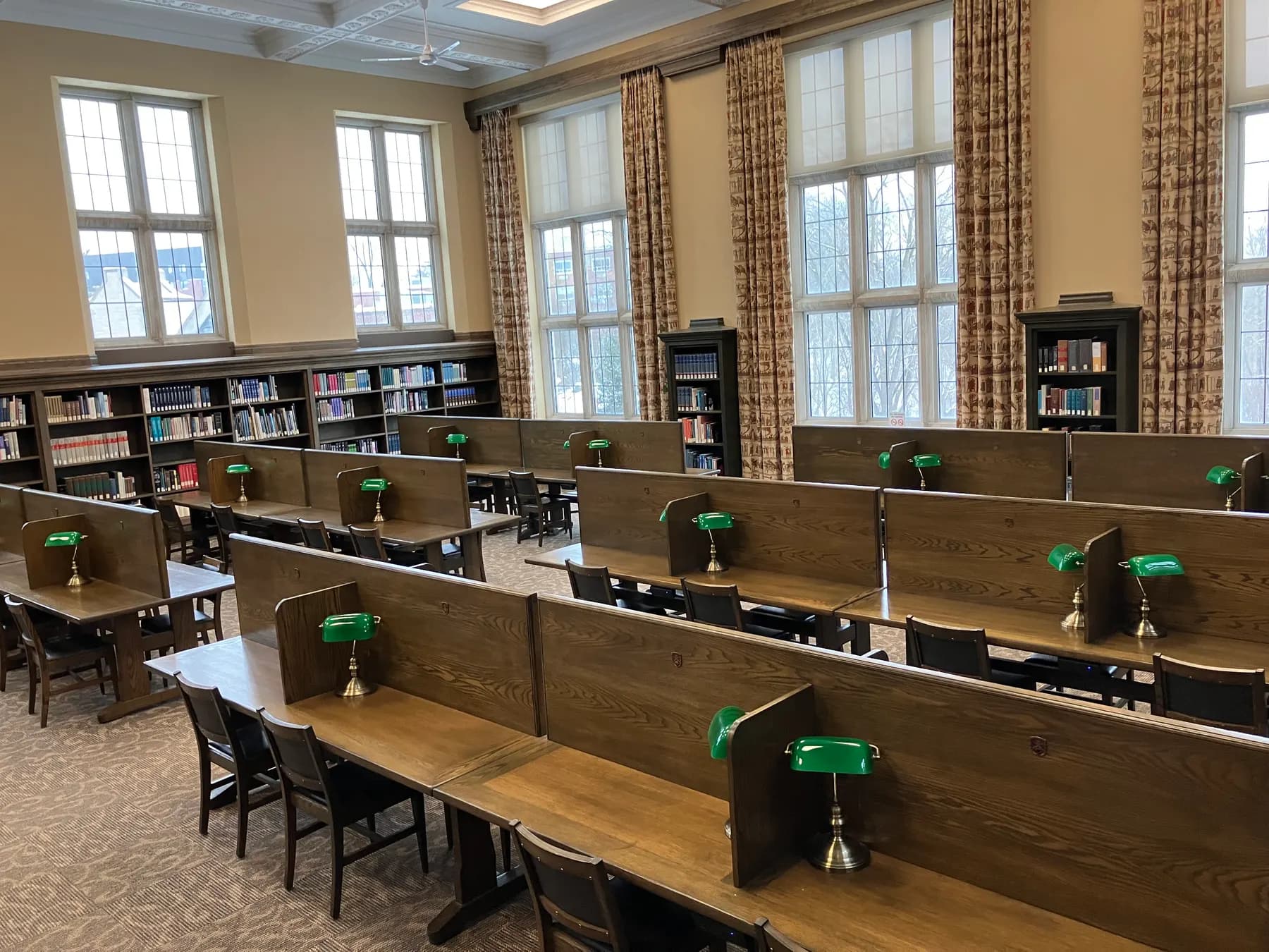 Wood study carrels with green reading lamps in a quiet, sunlit study room