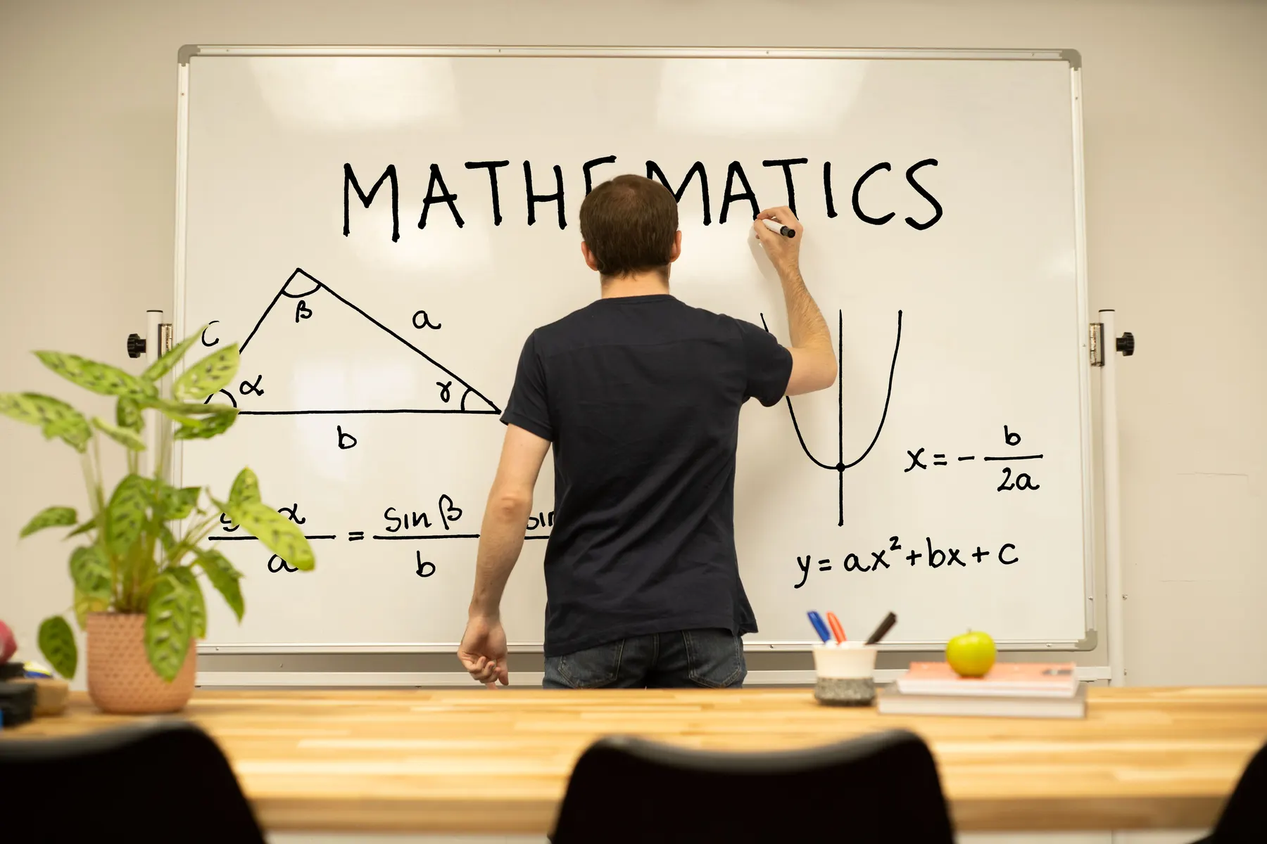 A tutor working through triangle and quadratic problems on a whiteboard at the study center