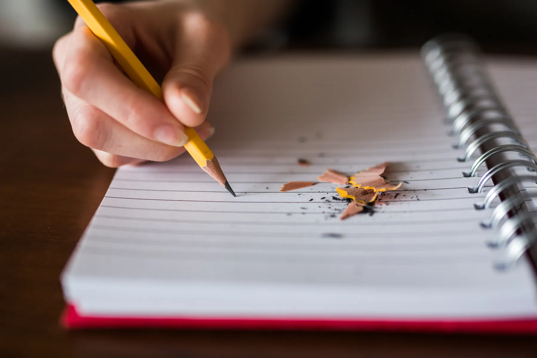 A hand writing in a spiral notebook with a sharpened pencil