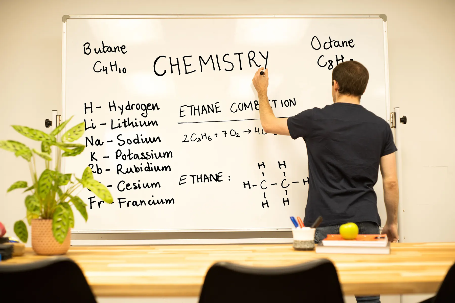 A tutor writing chemistry notation and an ethane combustion equation on a whiteboard